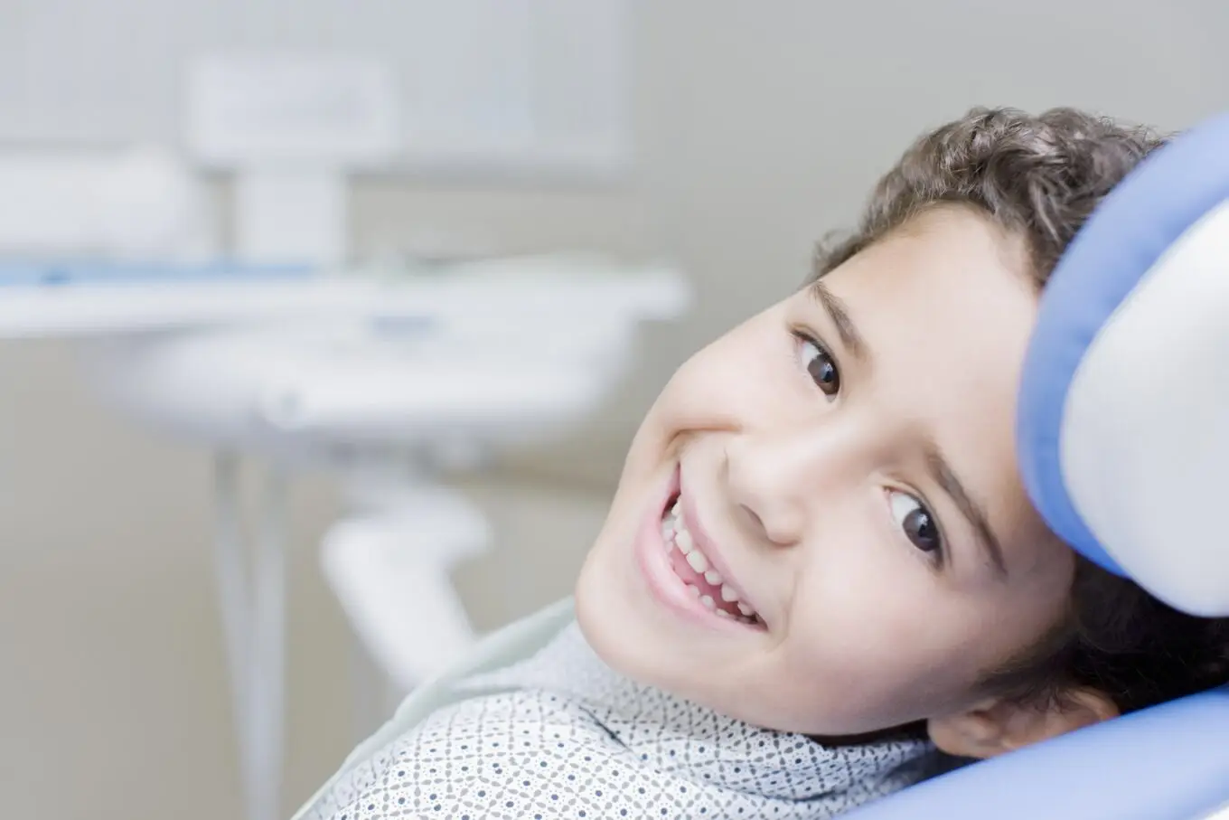 Young boy smiling in a dental chair, ready to receive dental sealants, promoting healthy teeth.