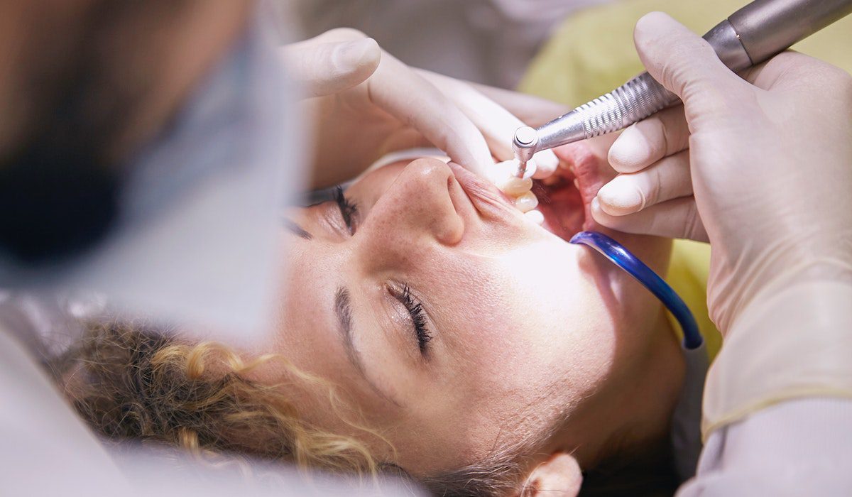 a dentist checking a woman's mouth with a dental handpiece