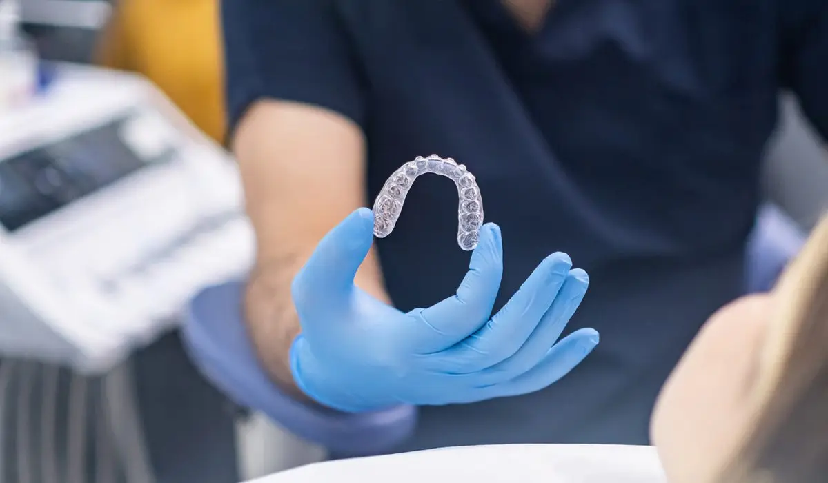 a hand wearing medical gloves holding a clear aligner