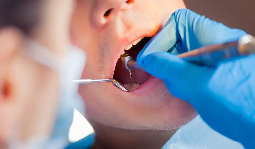 Dentist examining teeth of male patient with dental mirror and probe.