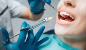Female client opens mouth as dentist holds instruments and syringe administers painkiller.