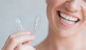 a woman with a perfect white teeth holding invisalign aligner
