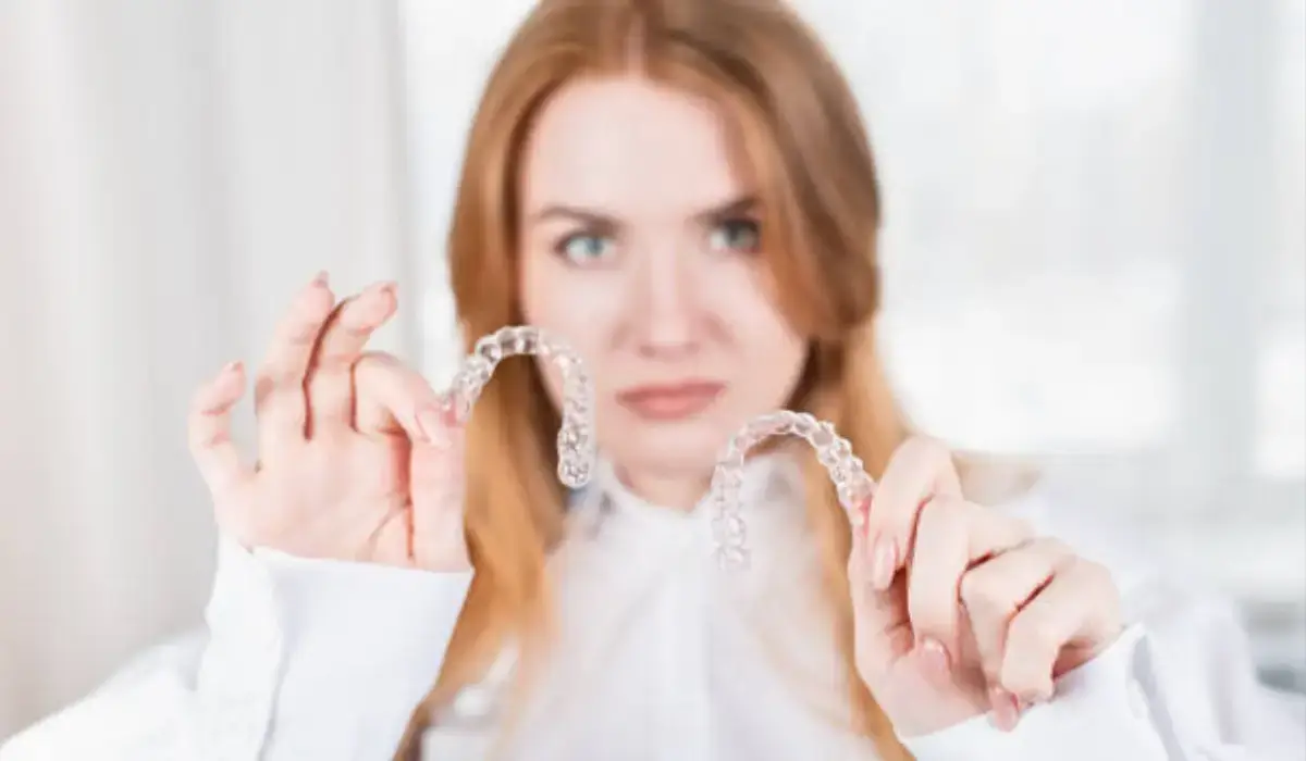 Frustrated woman holding two clear aligners, highlighting the quality differences between Invisalign and mail-order aligners.