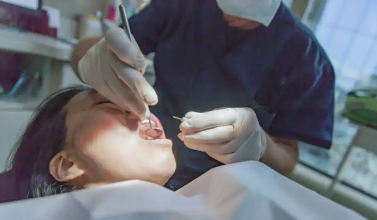 A dentist wearing gloves and a mask treating a patient with dental trauma using dental instruments in a clinic.