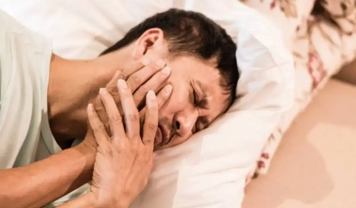 Man lying in bed holding jaw in pain, showing symptoms of a dental emergency or lockjaw.
