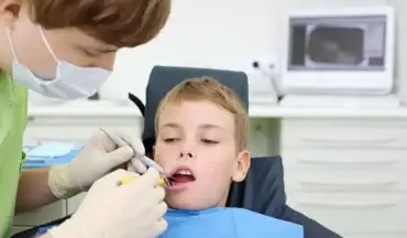 Pediatric dentist treating young boy for dental infection using scaler in modern clinic.