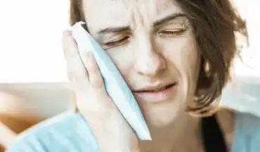 Woman applying cold compress to jaw due to tooth nerve pain.